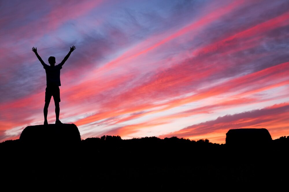 A man with arms outstretched to the sky at dusk.