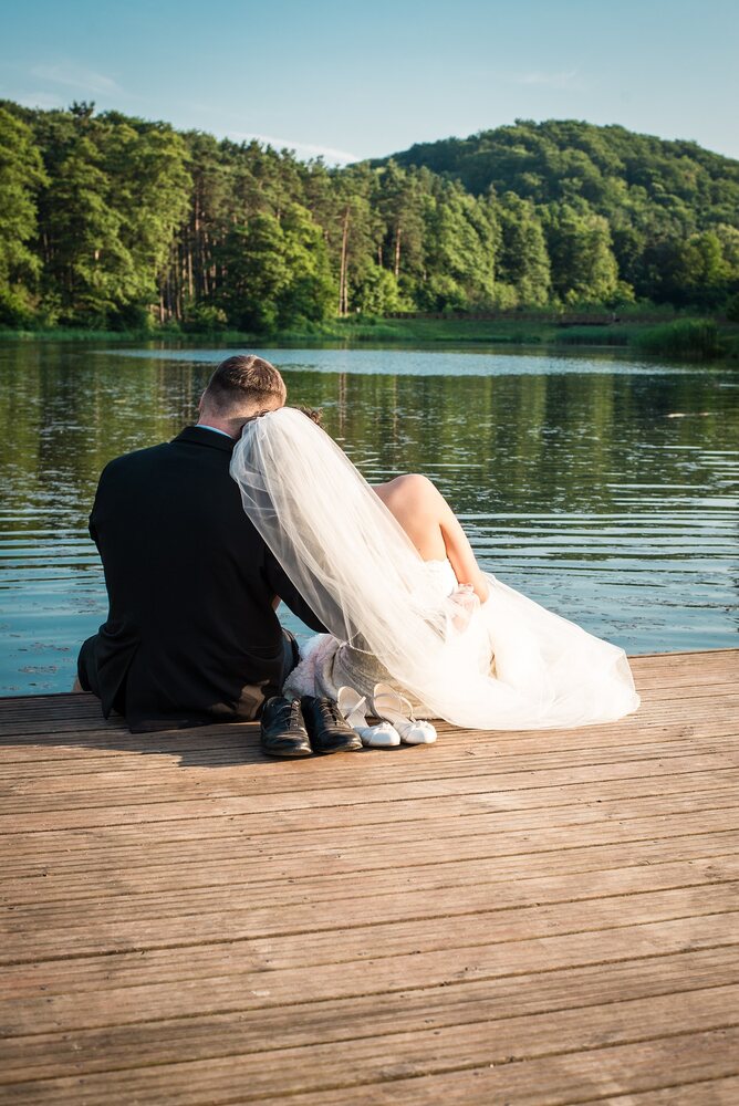 A couple married at a young age sitting on a boat dock overlooking a lake.