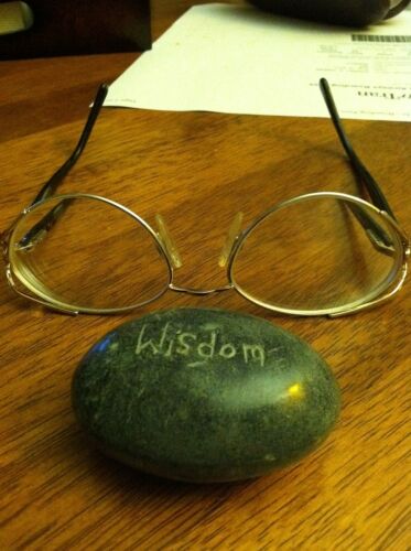 A rock next to a pair of glasses with the word “wisdom” inscribed on it.