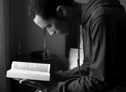 A man has his head down displaying humility as he reads a bible.