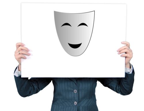 A person holds up a poster of a joyful, smiling mask in front of their face.