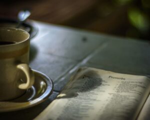 A Holy Bible opened to the book of Proverbs next to a cup of coffee.