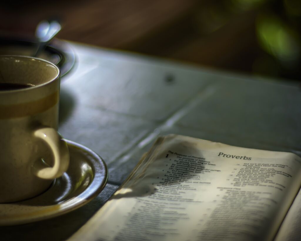 A Holy Bible opened to the book of Proverbs next to a cup of coffee.